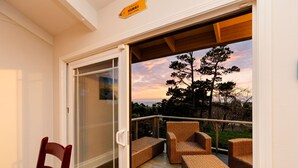 A covered outdoor deck with wicker furniture and a glass door leading to a scenic view. - Coast & Course  *Adventure Basecamp*Beach Access* (Lincoln Beach)