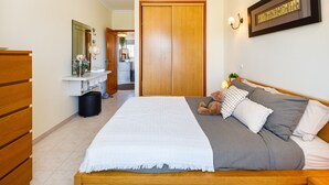 A bedroom with a large bed, a wooden dresser, a mirror, a framed picture, and a teddy bear.