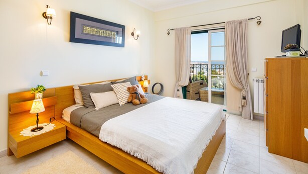 A modern bedroom with a large bed, bedside lamps, a flat-screen TV, and a view of the outdoors.