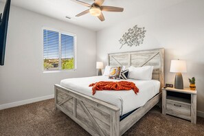 A bedroom with a wooden bed, a ceiling fan, a window with blinds, a nightstand with a lamp, and a decorative wall piece. - Ladera 379, Private Spa, Smart TVs, Community Pool (Washington)