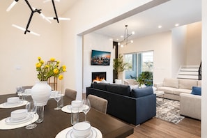 Een moderne woonkamer met een open haard, een eethoek met een vaas gele bloemen, en een trap naar een ander niveau.