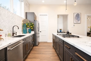 A modern kitchen with a marble countertop, stainless steel appliances, and a central island.