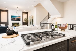 A modern kitchen with a gas stove, a marble countertop, and a dining area with a sofa and a tea set.