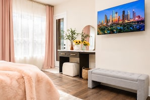 Une chambre à coucher avec un lit, un bureau doté d’un miroir, un banc et un tableau représentant un paysage urbain accroché au mur.