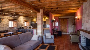 A rustic interior with a stone wall, wooden beams, a fireplace, and a dining area. - Country House 'La Cajola' with Mountain View, Private Pool and Wi-Fi (Lladurs)