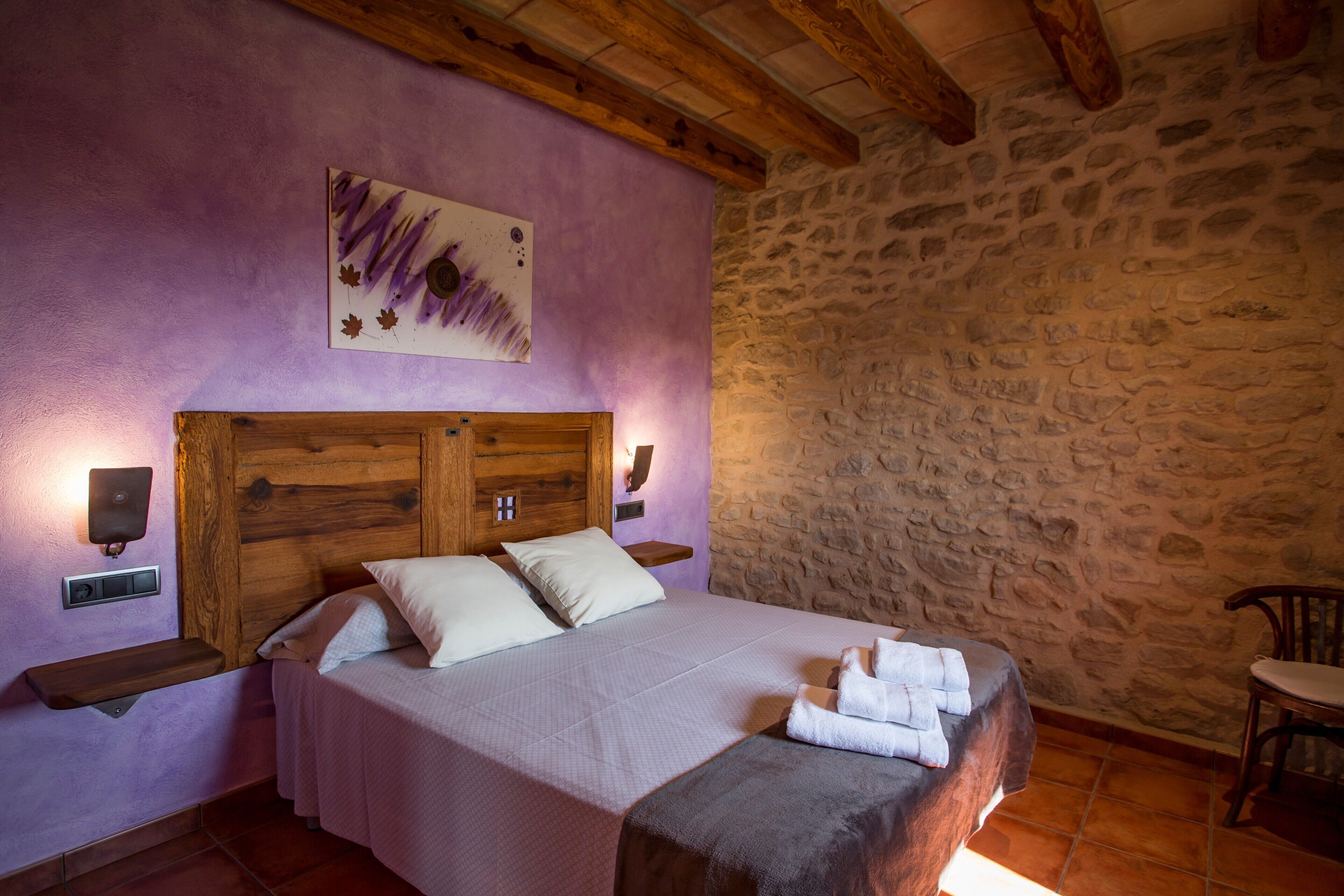 Un dormitorio con pared de piedra, cabecera de madera y cama con ropa de cama blanca.