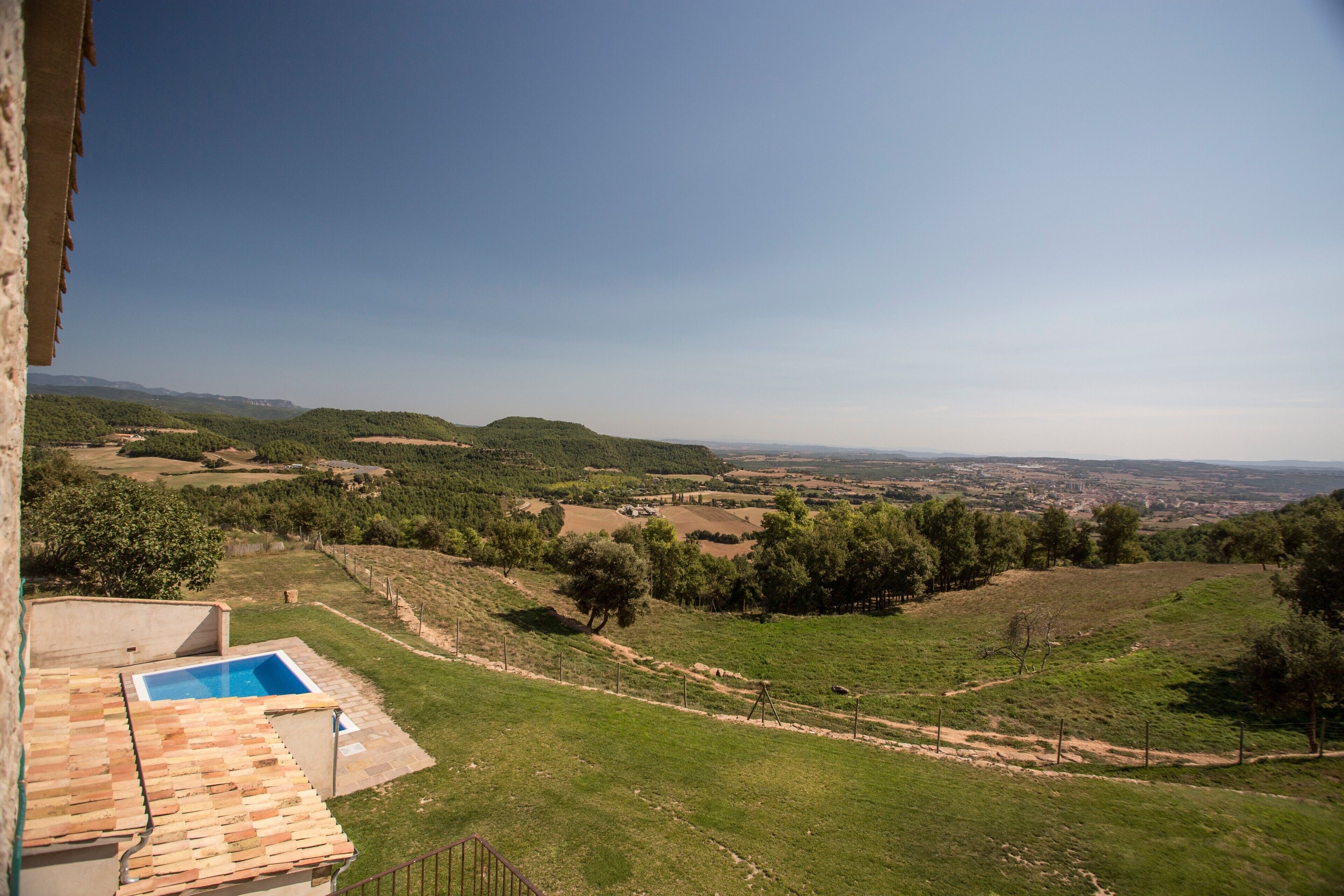 Vista de un paisaje montañoso con piscina y un edificio de techo con tejas.