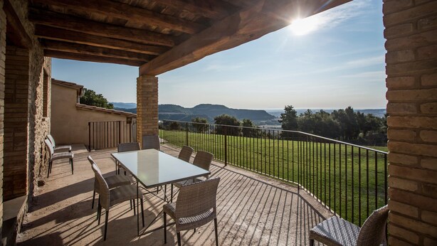 A covered patio with a table and chairs, a brick wall, and a view of a green landscape. - Country House 'La Cajola' with Mountain View, Private Pool and Wi-Fi (Lladurs)