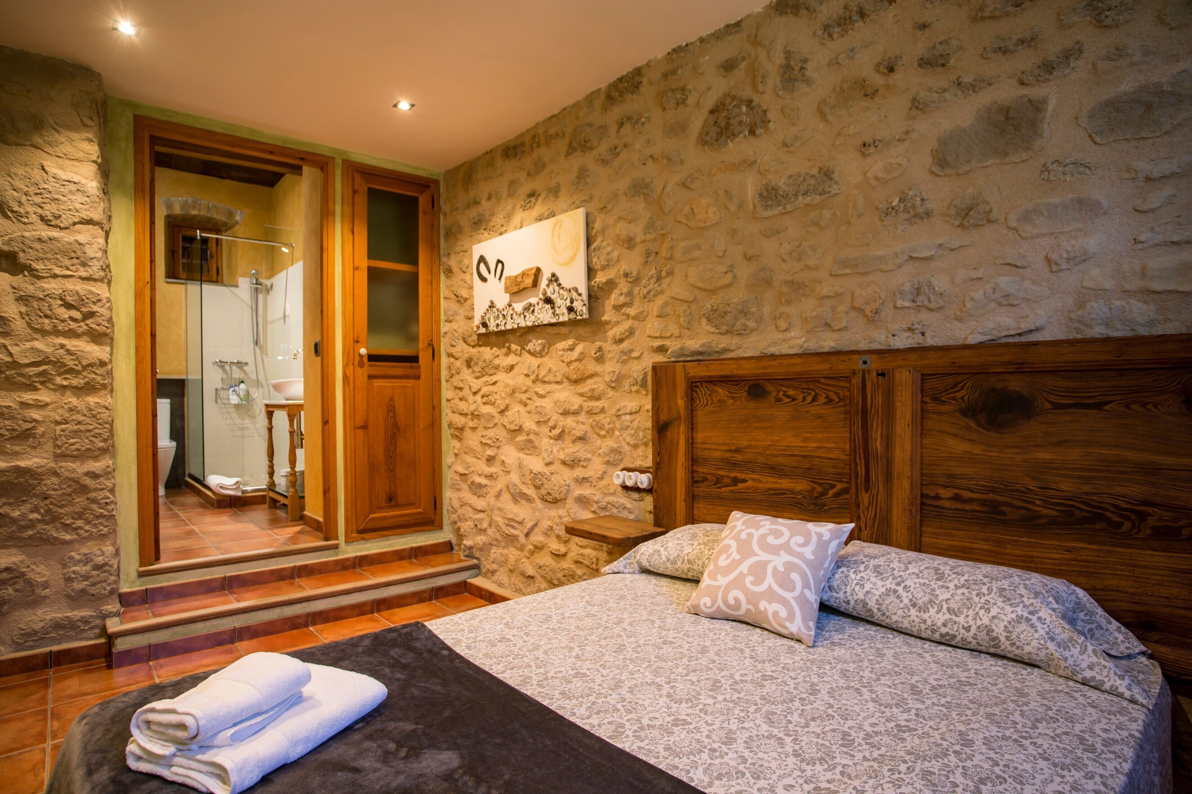 A bedroom with a stone wall, wooden door, and a bed with patterned bedding.
