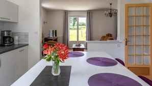 Una cocina moderna con cafetera, una mesa de comedor con individuales morados y un jarrón con flores.