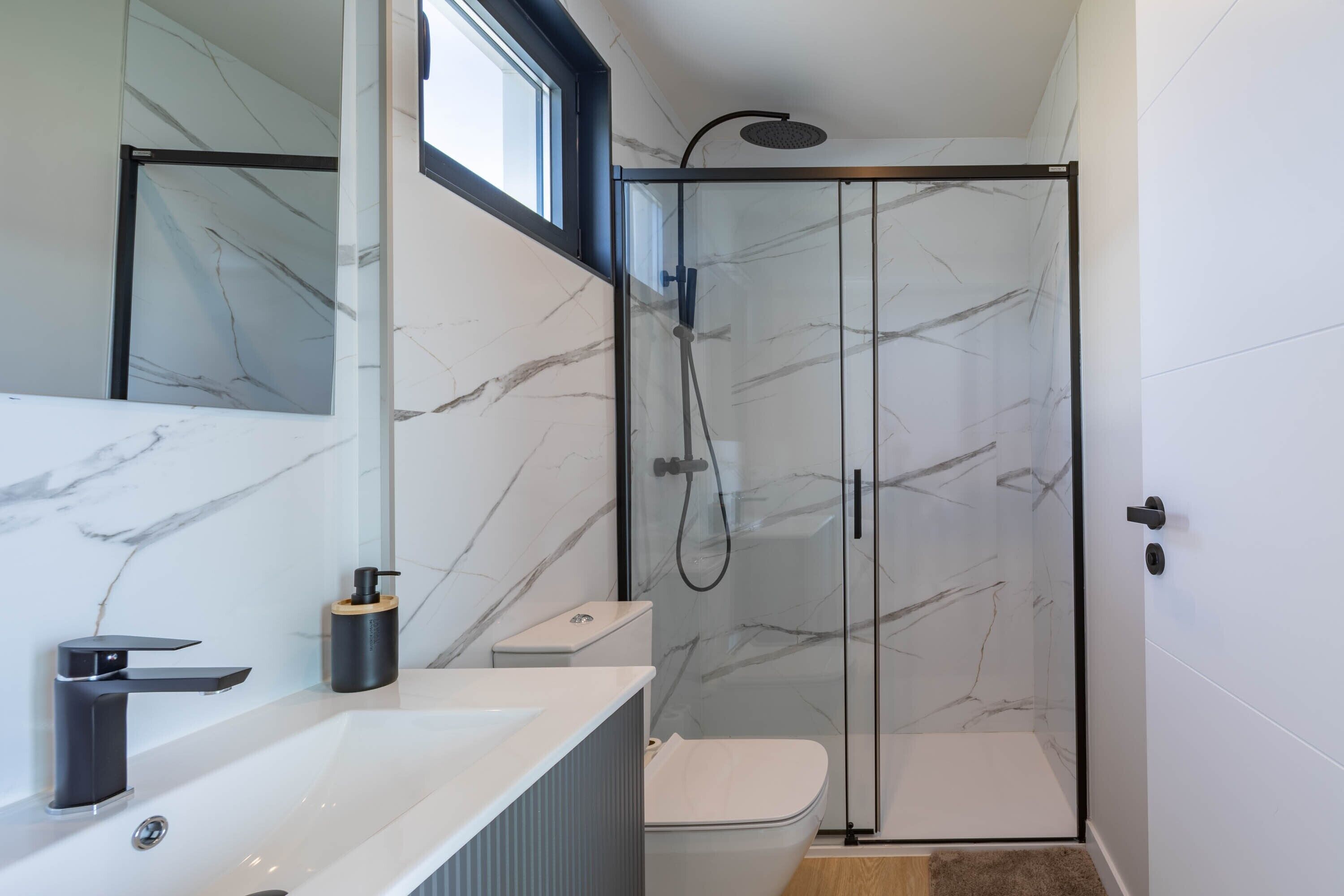 Un baño moderno con ducha de vidrio, lavamanos blanco y retrete.