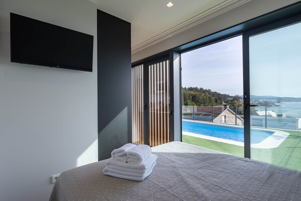 Un dormitorio con cama, televisor, vista a una piscina y balcón.