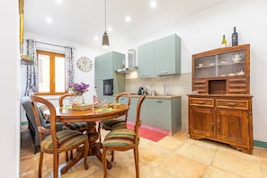 Un coin repas avec une table et des chaises en bois, une cuisine avec des meubles verts et un buffet en bois doté de portes en verre.