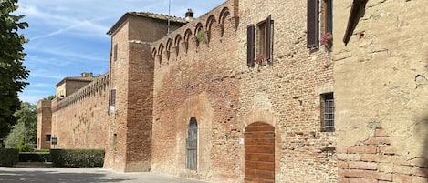 A historic building with arched windows and a central door, surrounded by a paved courtyard.