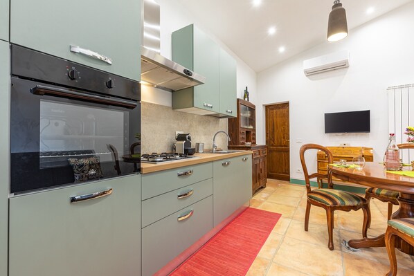 Una cocina con estufa, horno y armarios; un comedor con mesa y sillas; un televisor en la pared; y un equipo de aire acondicionado.