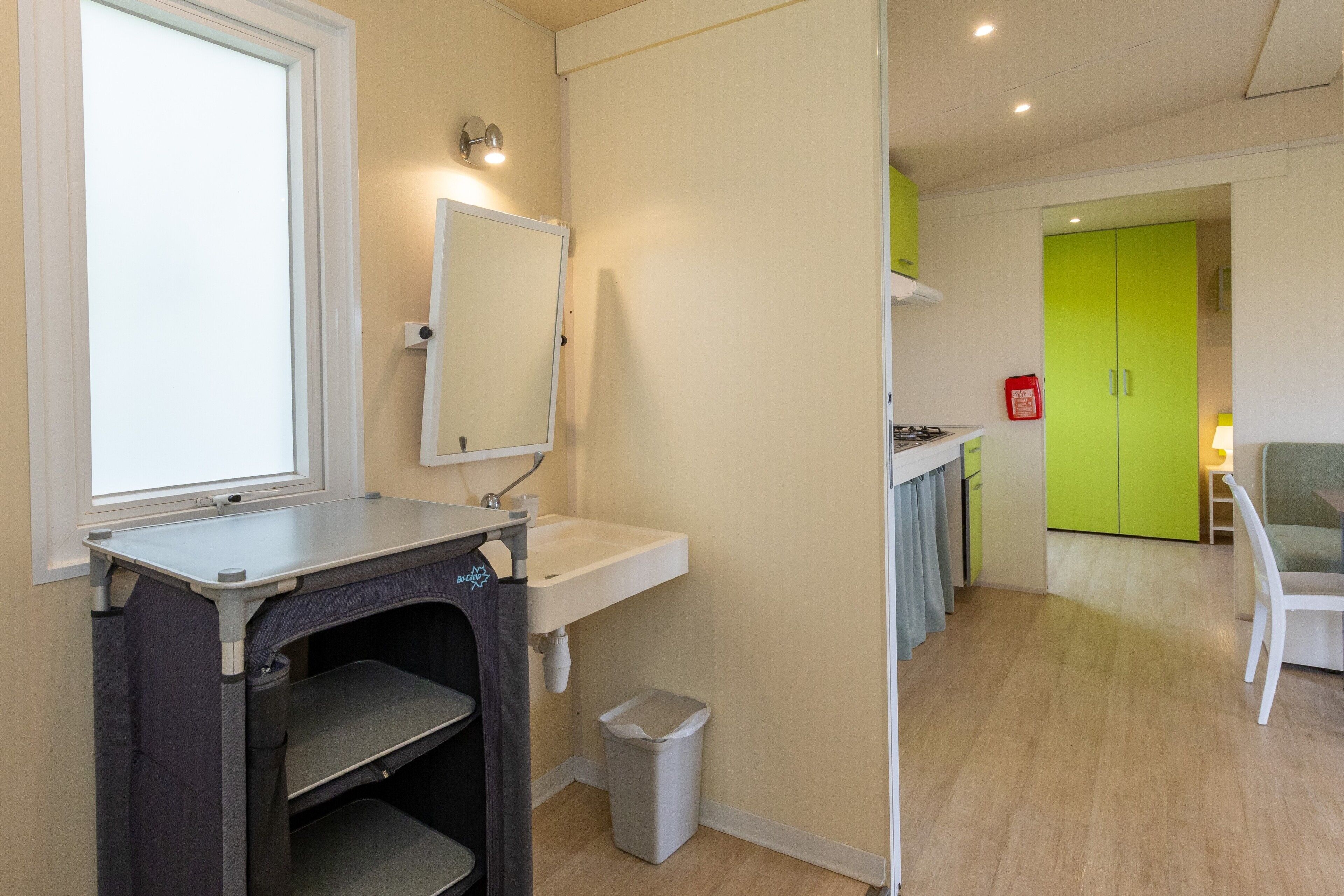 A modern kitchen with a sink, mirror, and a trash bin.