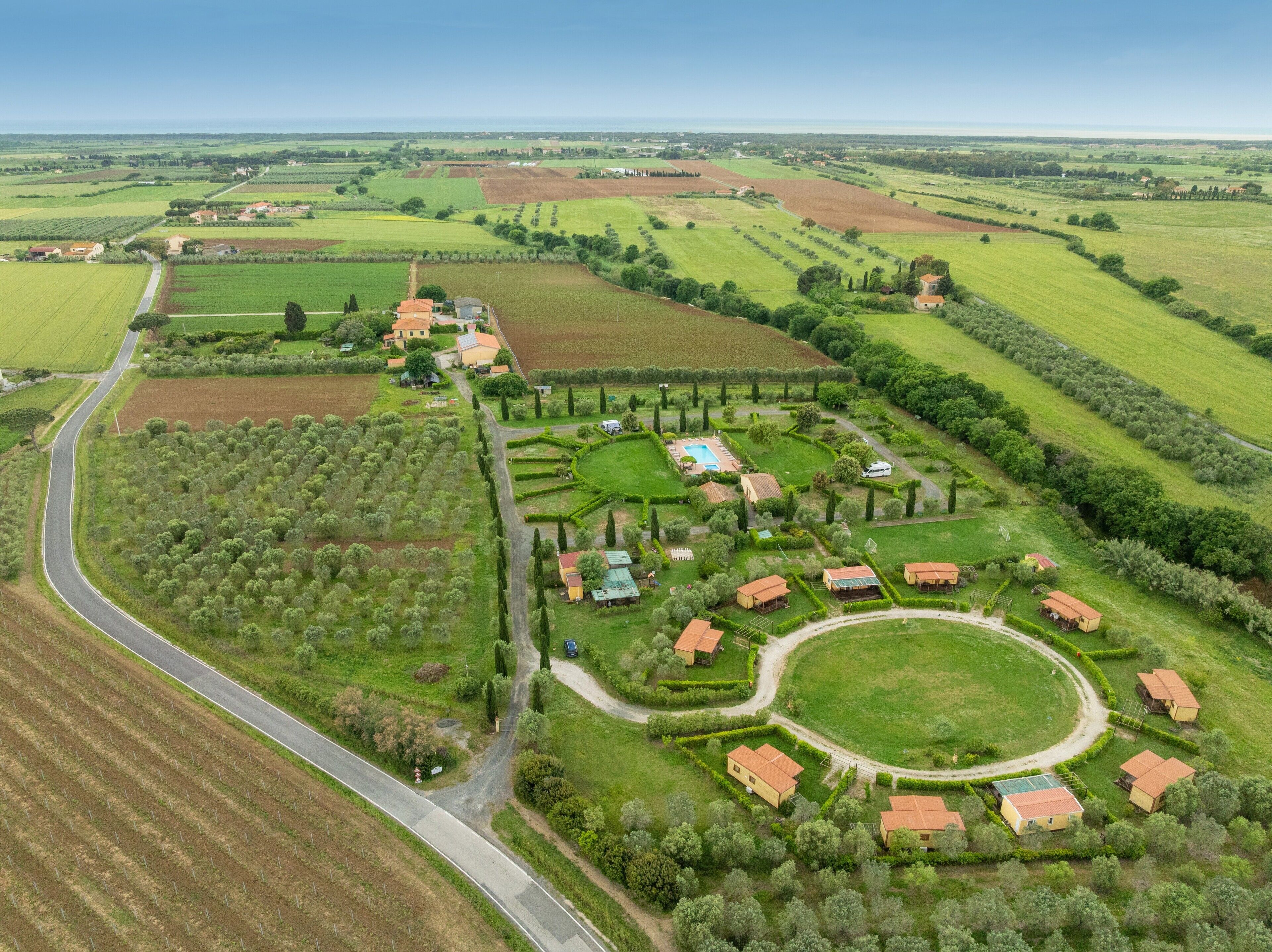 An aerial view of a countryside property with a winding road, green fields, and several buildings with red roofs.