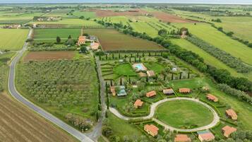 An aerial view of a countryside property with a winding road, green fields, and several buildings with red roofs.