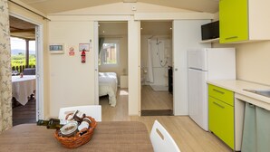Eine kleine Küche mit Kühlschrank, Mikrowelle und Spüle. Ein Essbereich mit Tisch und Stühlen lädt zum Verweilen ein, und ein Fenster bietet Blick auf einen Garten.