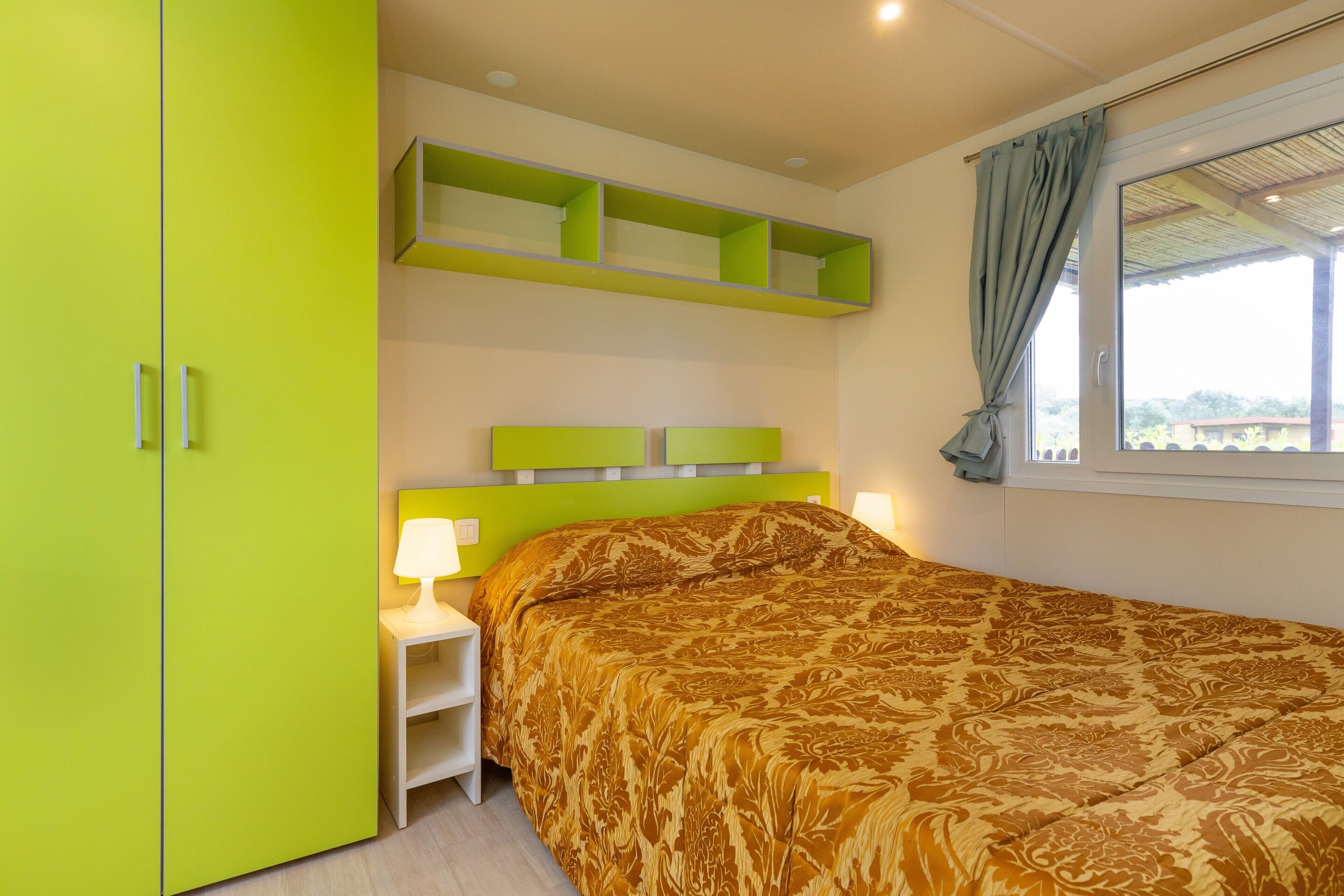 Een slaapkamer met een bed, een nachtkastje, een groene kast en een raam met gordijnen.