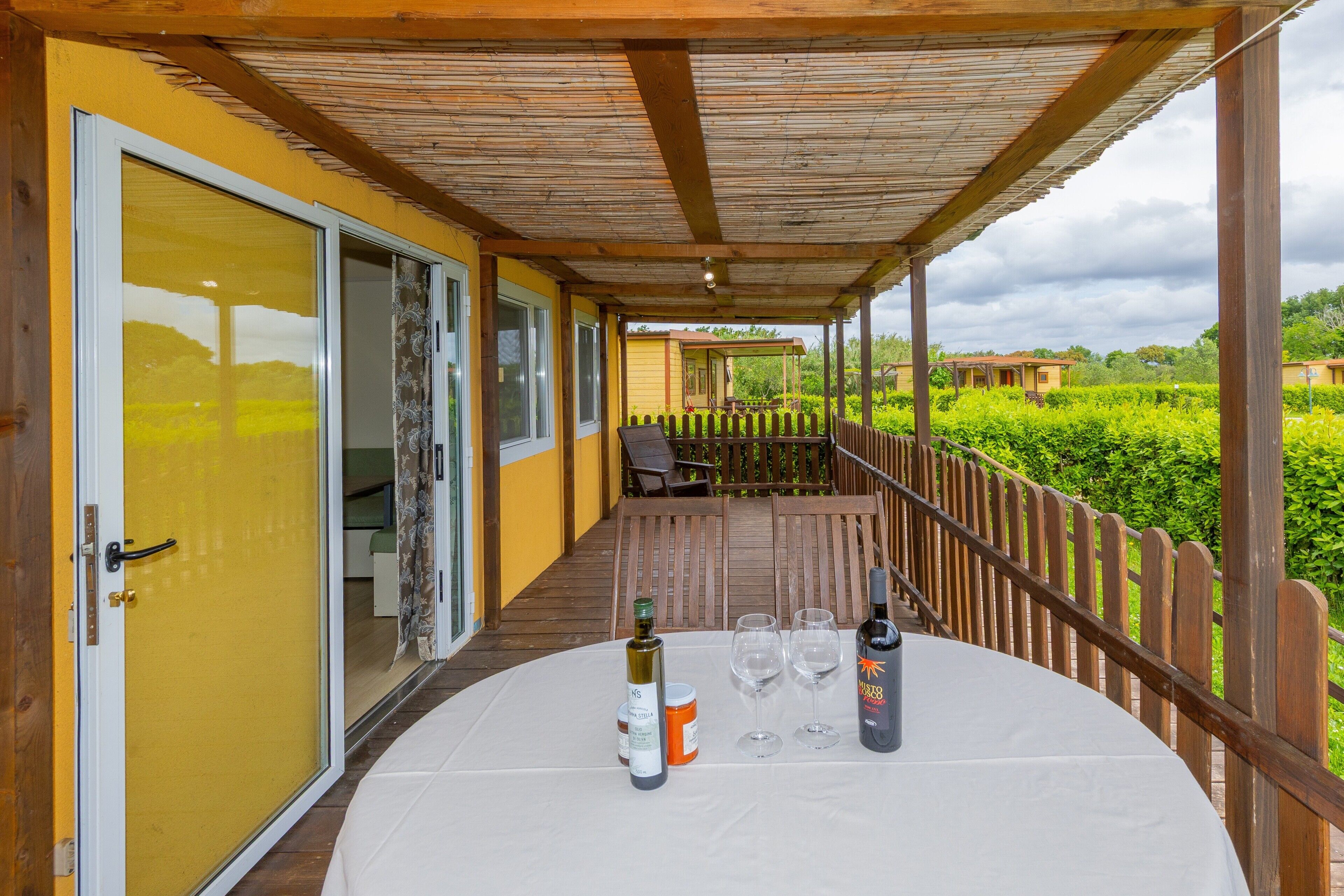 A covered outdoor area with a table set for dining, a bottle of wine, and wine glasses.