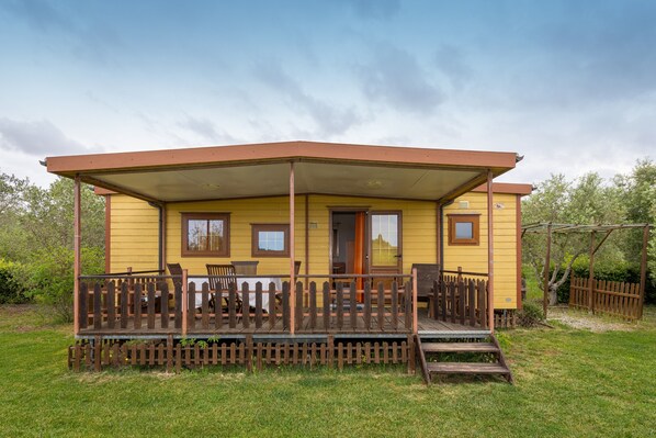 Un bâtiment jaune doté d’un porche couvert, d’une clôture en bois et d’une petite terrasse.