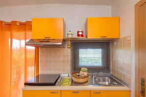Una cocina compacta con estufa a gas, lavamanos y ventana con persianas.