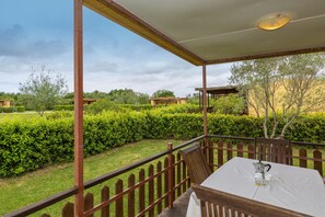 Un espace extérieur abrité, avec une table et des chaises, entouré d’une clôture en bois et de verdure.