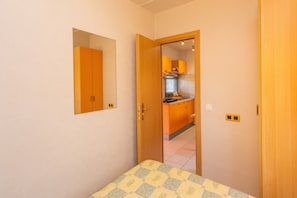 Quarto com cama, porta para uma cozinha e espelho na parede.