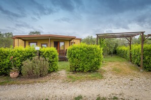 Un bâtiment jaune doté d’un porche abrité, entouré de haies verdoyantes et bordé d’un chemin de gravier.