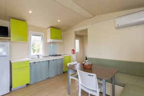 A compact kitchen with a sink, stove, and green cabinets. There is a dining table with chairs and a green sofa.