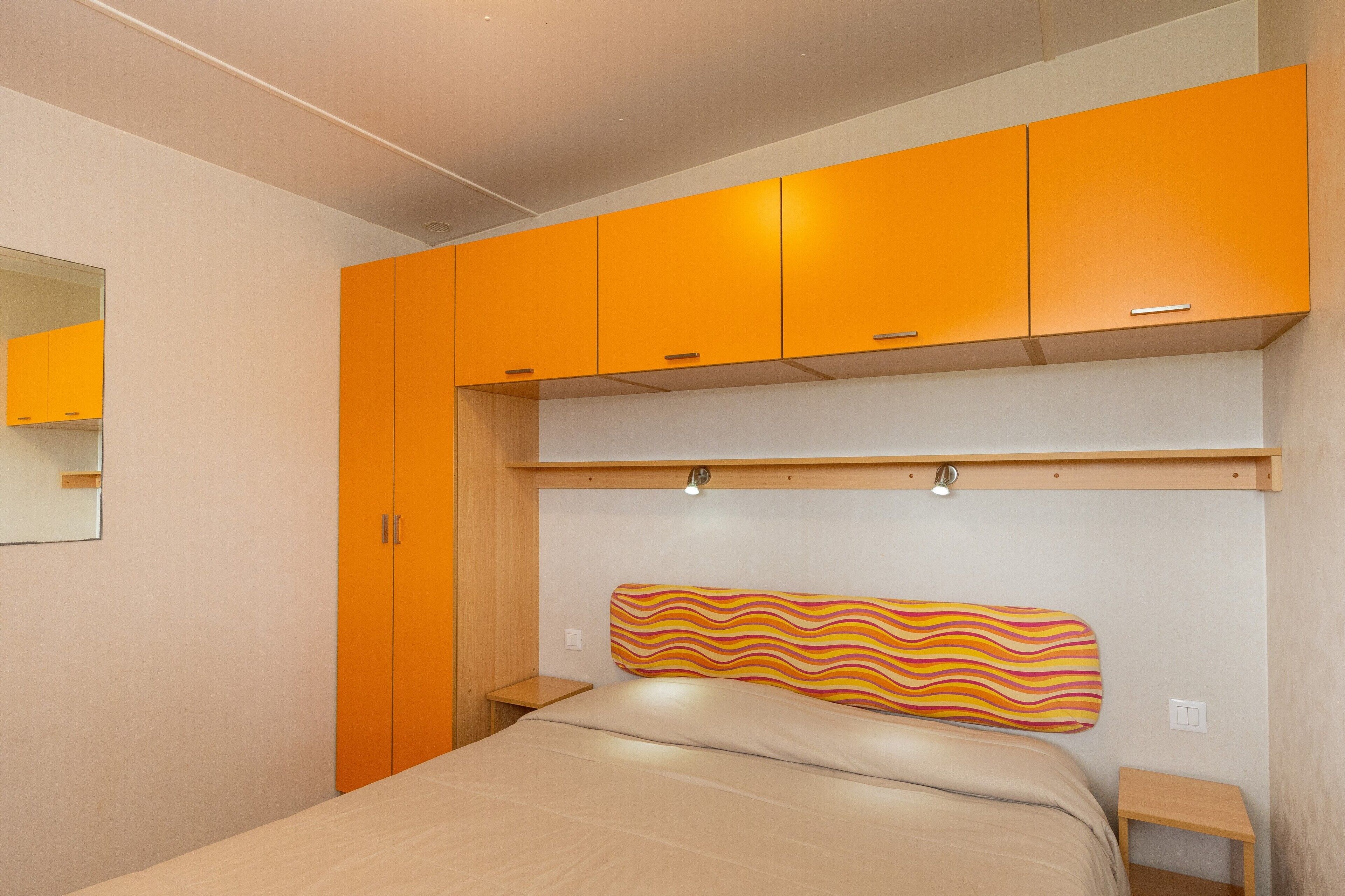 A bedroom with a bed, a headboard, a nightstand, and orange cabinets.