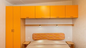 Een slaapkamer met een bed, oranje kastjes en een gestreept hoofdeinde.