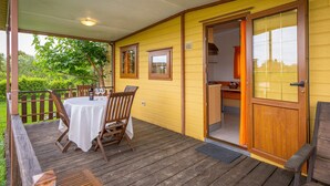 Een overdekt terras met een houten vloer, een tafel met stoelen en een deur naar een binnenruimte.