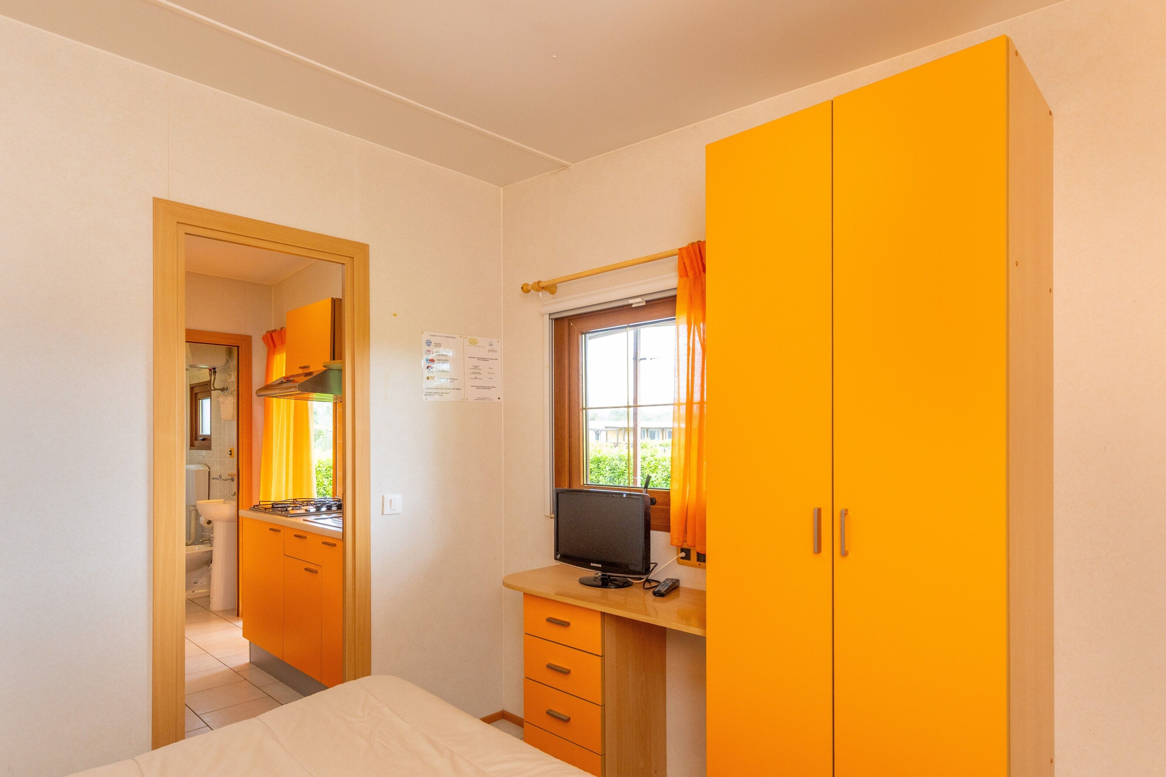 A bedroom with a bed, a desk with a computer, and a window with curtains.