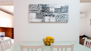 Comedor con una mesa de vidrio, sillas blancas y una obra de arte abstracta colgada en la pared.
