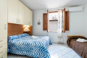 Un dormitorio con cama, armario, lámpara de noche y ventana con cortinas.