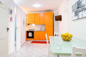 A modern kitchen with orange cabinets, a glass dining table, and a bowl of lemons.