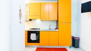 Una cocina compacta con armarios color naranja, un horno negro y una alfombra roja.