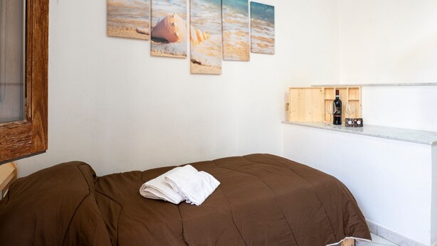 Un dormitorio con cama, ventana y estante con una botella y vasos.