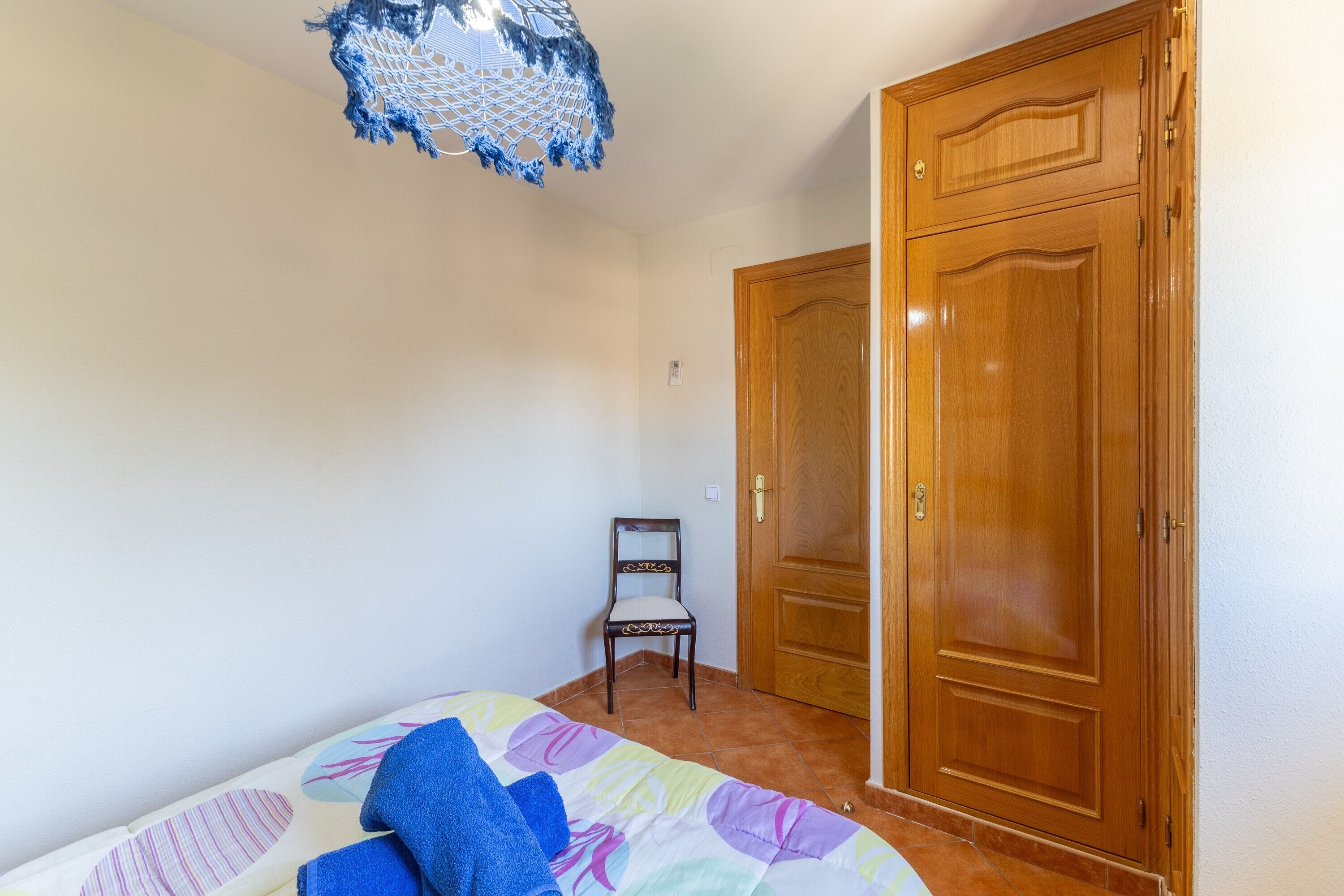 A bedroom with a bed, a chair, a wooden wardrobe, and a ceiling light fixture.