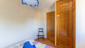 A bedroom with a bed, a chair, a wooden wardrobe, and a ceiling light fixture.
