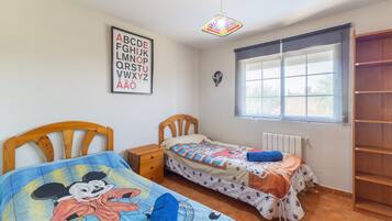 Un dormitorio con dos camas individuales, una ventana con persianas, un radiador, un armario de madera y un cartel del alfabeto colgado en la pared.