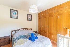 A bedroom with a bed, wooden wardrobe, and two framed artworks on the wall.