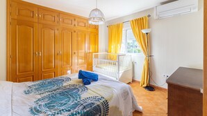 A bedroom with a bed, a crib, wooden wardrobes, a hanging light fixture, and a window with curtains. - Holiday Home 'Villa Pilara - Brunete' with Private Pool, Wi-Fi and Air Conditioning (Brunete)