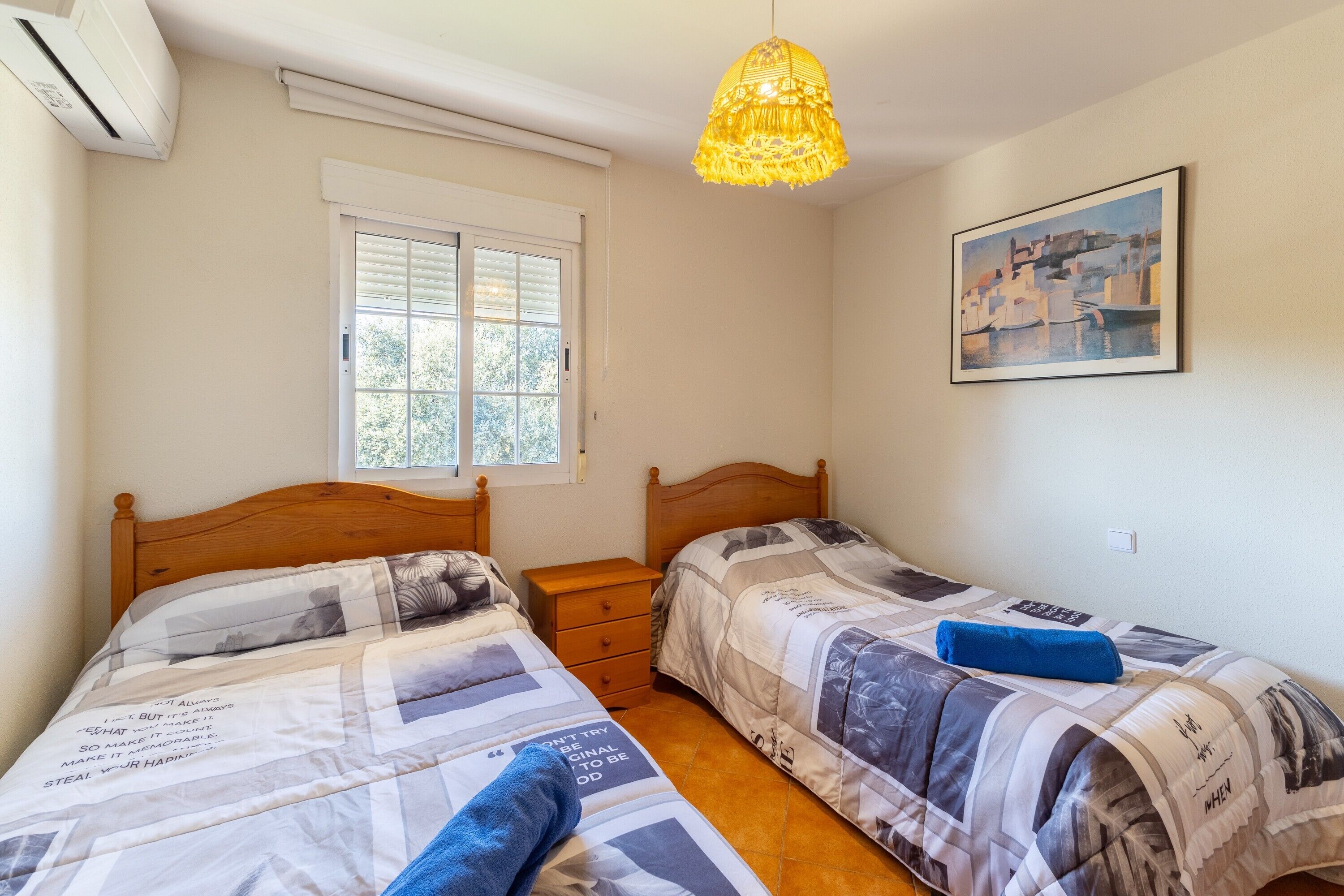 Un dormitorio con dos camas, una ventana, un cuadro y una lámpara colgante.
