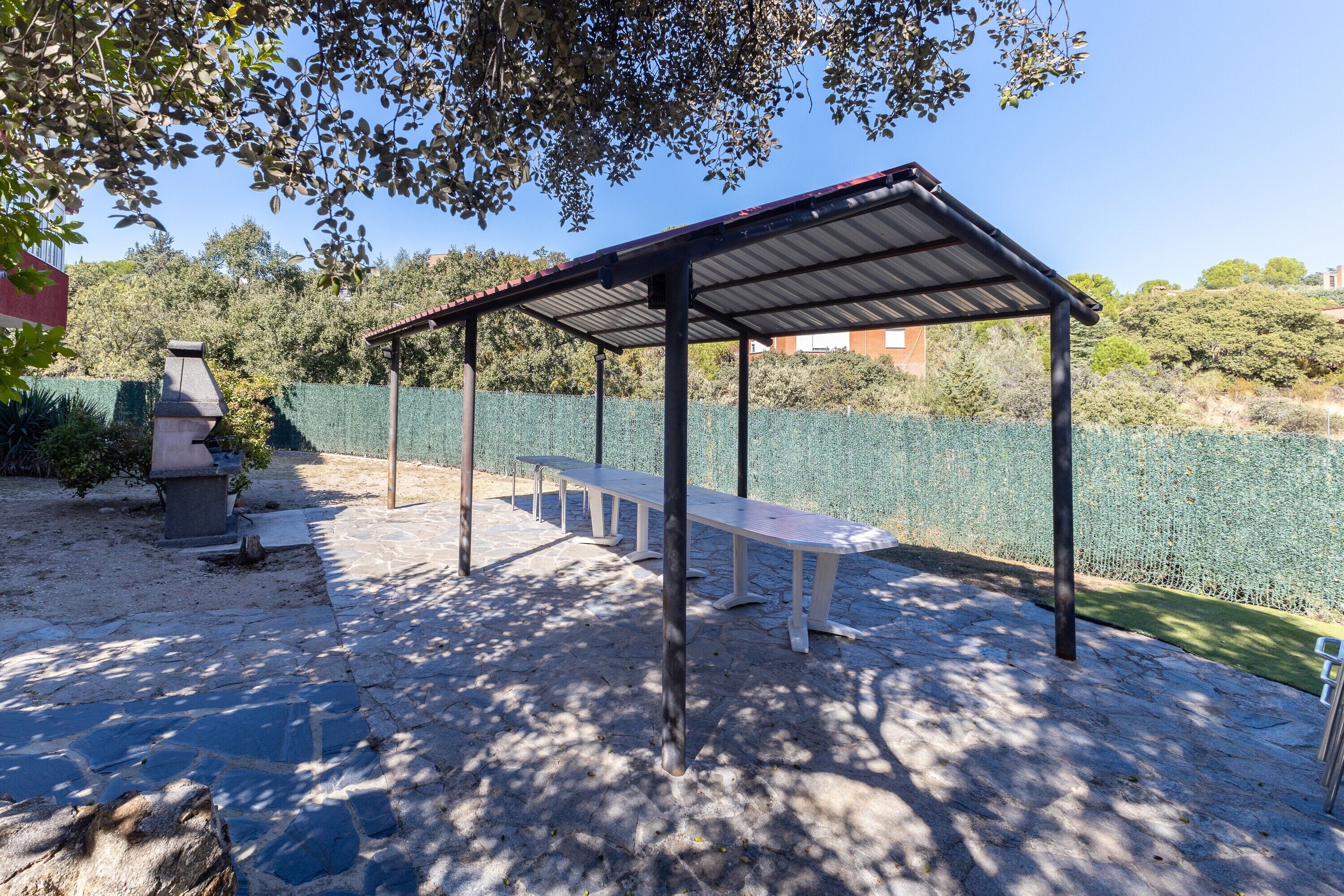 Een overdekt terras met stenen vloer, een barbecue en een bank.