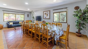 Un comedor con una mesa dispuesta para seis personas, rodeada de sillas de madera, un sofá y un televisor.