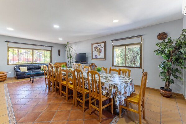 Un comedor con una mesa dispuesta para seis personas, rodeada de sillas de madera, un sofá y un televisor.