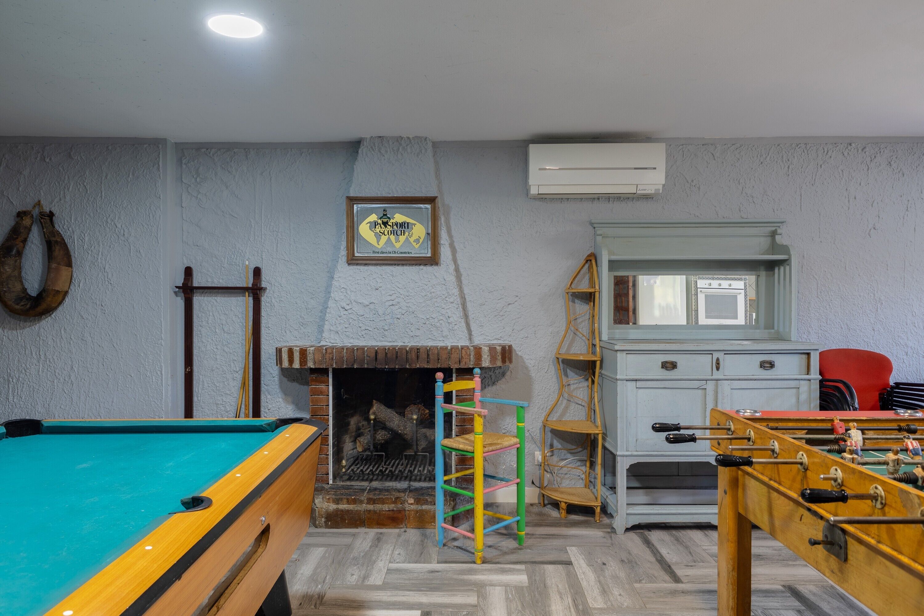 Een kamer met een pooltafel, een tafelvoetbaltafel, een open haard en een bord waarop 'Passport Scotch' staat.